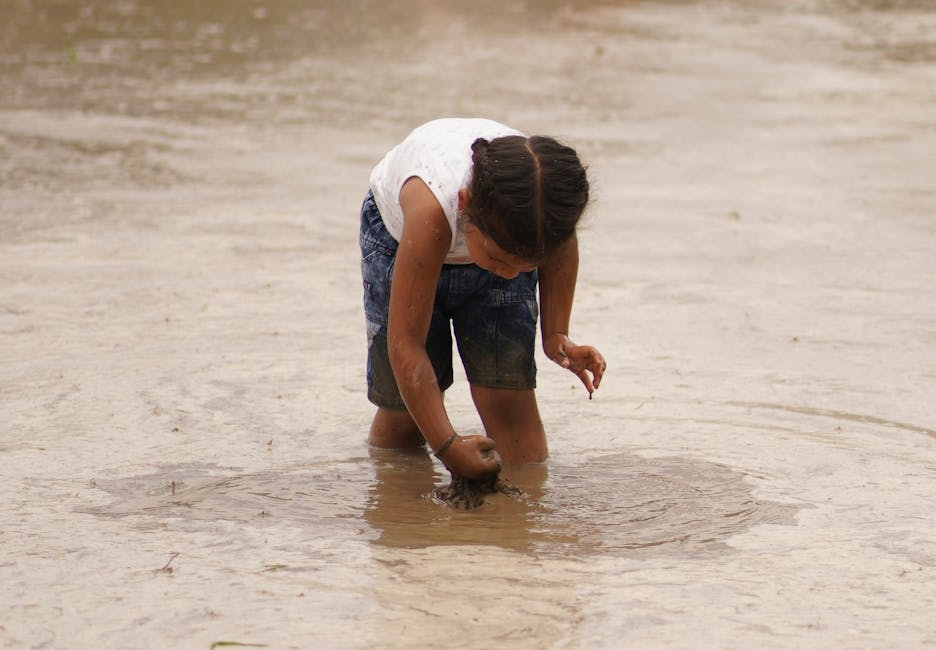 A young child exploring and playing in a mud puddle outdoors, enjoying nature.